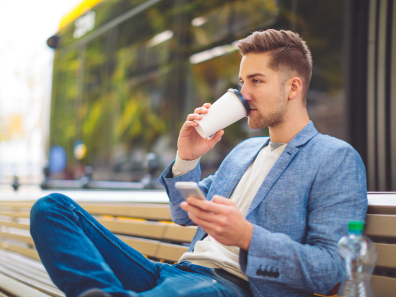 A man sitting on a bench, drinking from a coffee cup.